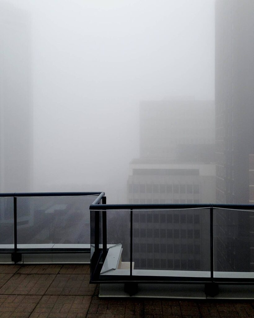 Quiet, foggy city view seen from behind an apartment balcony railing.