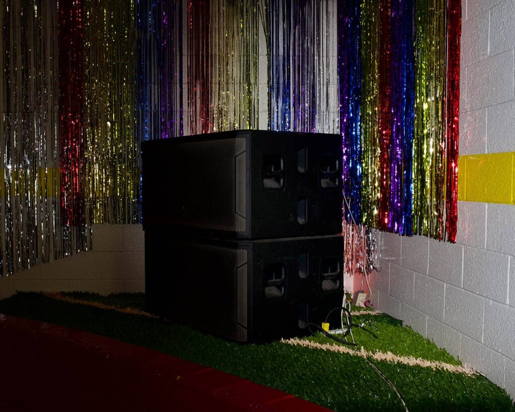 Two large black speakers stacked in the corner of a roller rink with streamers behind them.