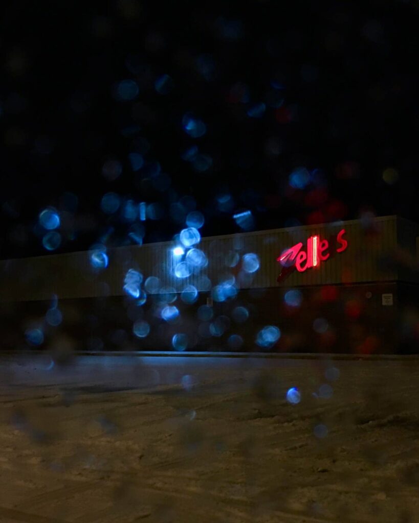 A red neon Zellers sign peaks through a wet car window on a stormy night.